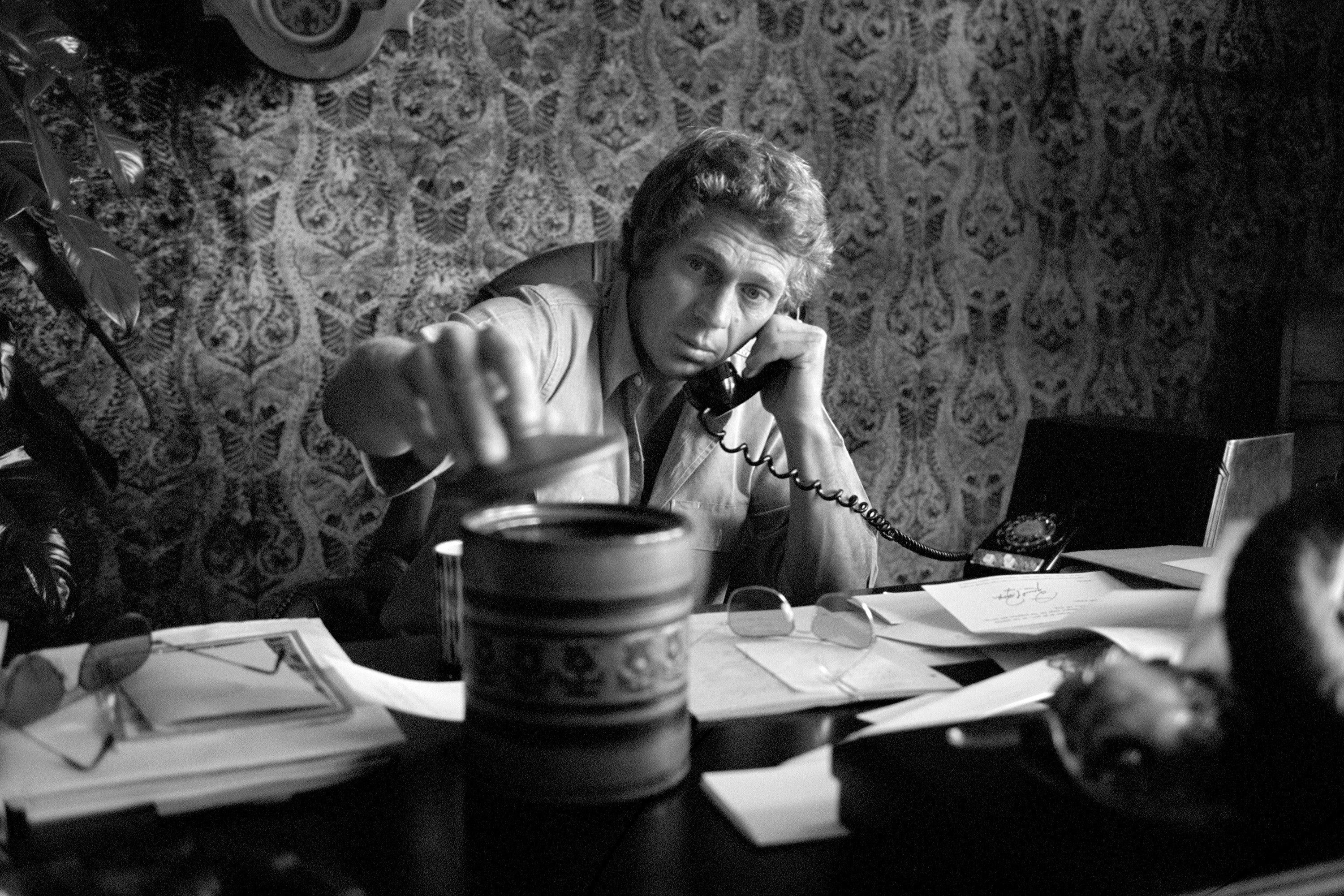 American actor Steve McQueen sitting on his desk in his Hollywood office, making a phone call. 1969.