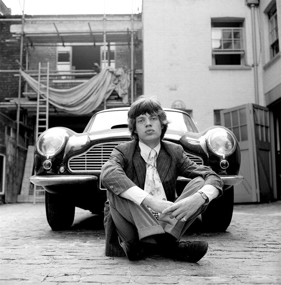 Mick Jagger sitting in front of his 1965 Aston Martin DB6.