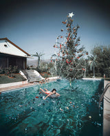 Rita Aarons, wife of photographer Slim Aarons, swimming in a pool festooned with floating baubles and a decorated Christmas tree, Hollywood, California, 1954.