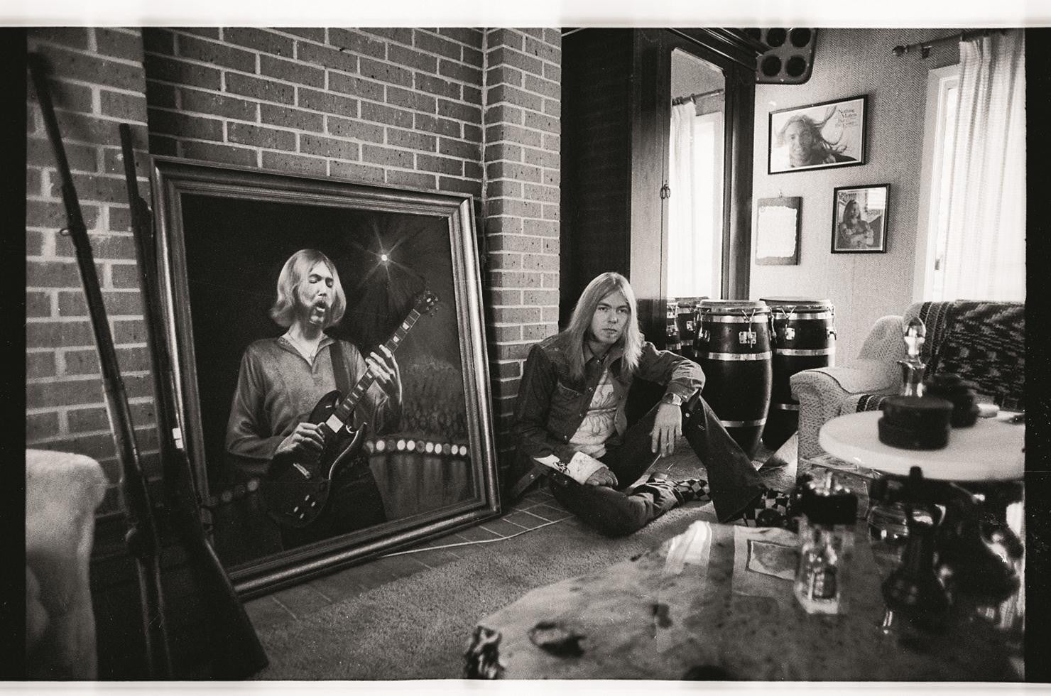 Gregg Allman sitting in front of a portrait of his late brother Duane in Macon, GA. 1975