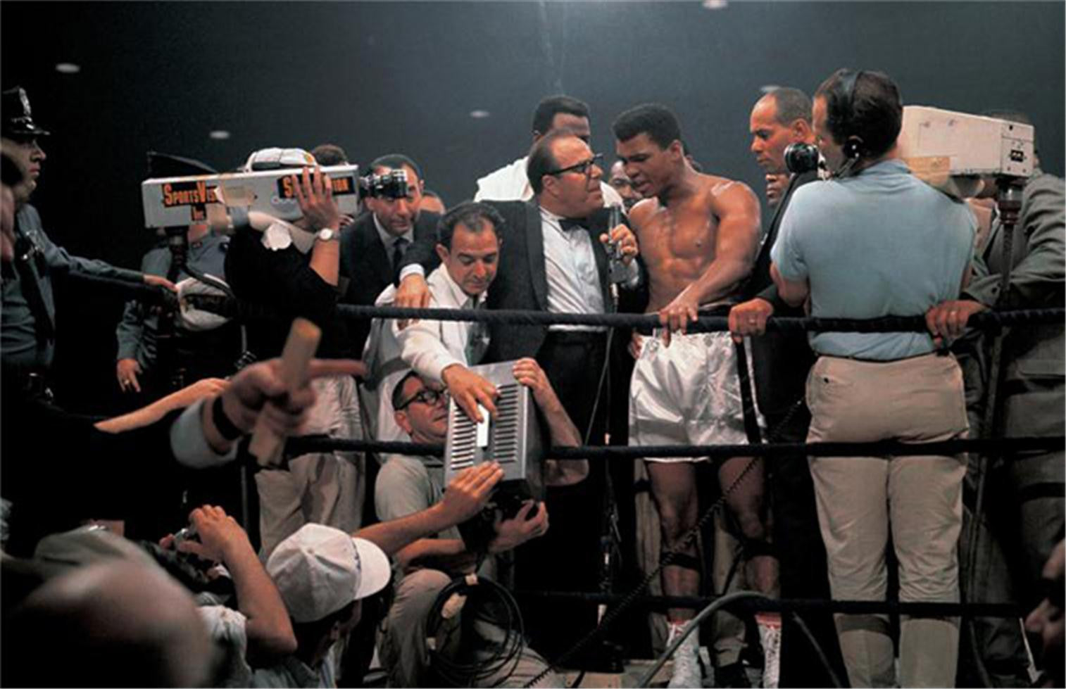 May 25th, 1965 - Muhammad Ali with media while trainer Angelo Dundee watches the instant replay of knockout, after winning fight vs. Sonny Liston at St. Dominick Arena in Lewiston, Maine.