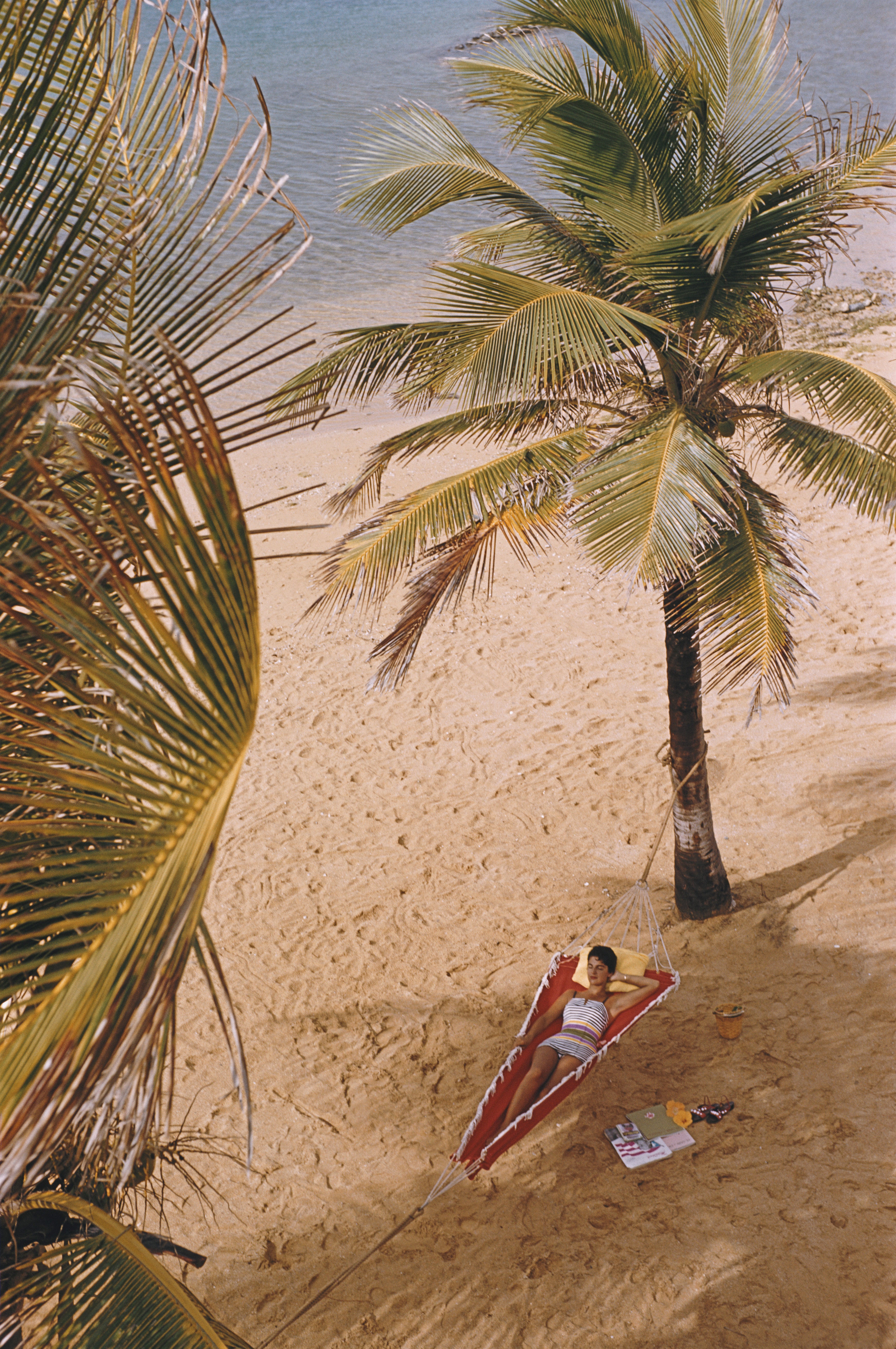 A woman reclining in a hammock hung between palm trees on the beach at the Caribe Hilton in San Juan, Puerto Rico, March 1956.