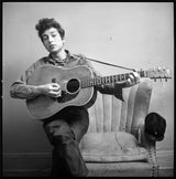 Bob Dylan sitting on his couch &amp; strumming his guitar at his West 4th Street apartment, NYC, 1963